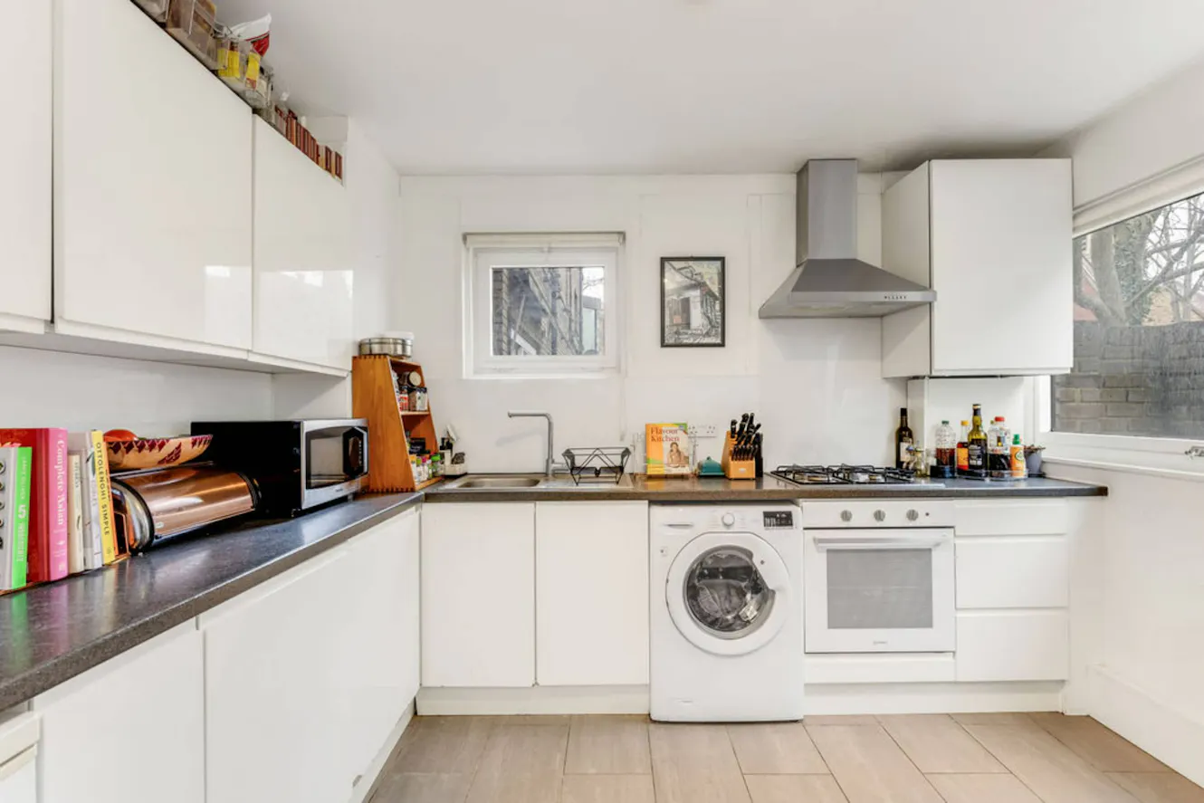 Kitchen with white cabinets, dark countertops, gas stove, stainless steel range hood, sink, washing machine, microwave, and window with natural light