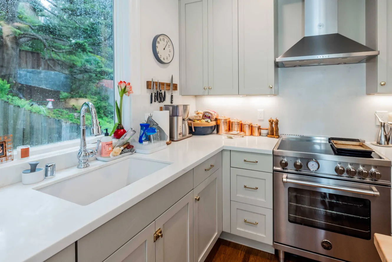 Kitchen with light gray cabinets, white quartz countertops, stainless steel appliances, undermount sink, and large window with garden view