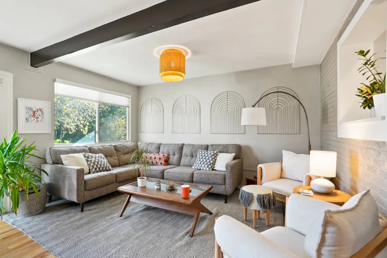 Living room with gray sectional sofa, white accent chairs, wooden coffee table, large window with natural light, and decorative wall art