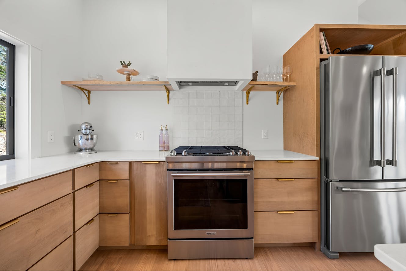 Kitchen with light wood cabinets, white countertops, stainless steel appliances including gas range and refrigerator, white tile backsplash, and open shelving