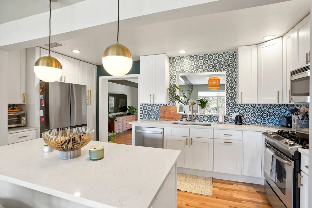 Kitchen with white cabinets, quartz countertops, stainless steel appliances, decorative blue patterned backsplash, pendant lighting, and center island