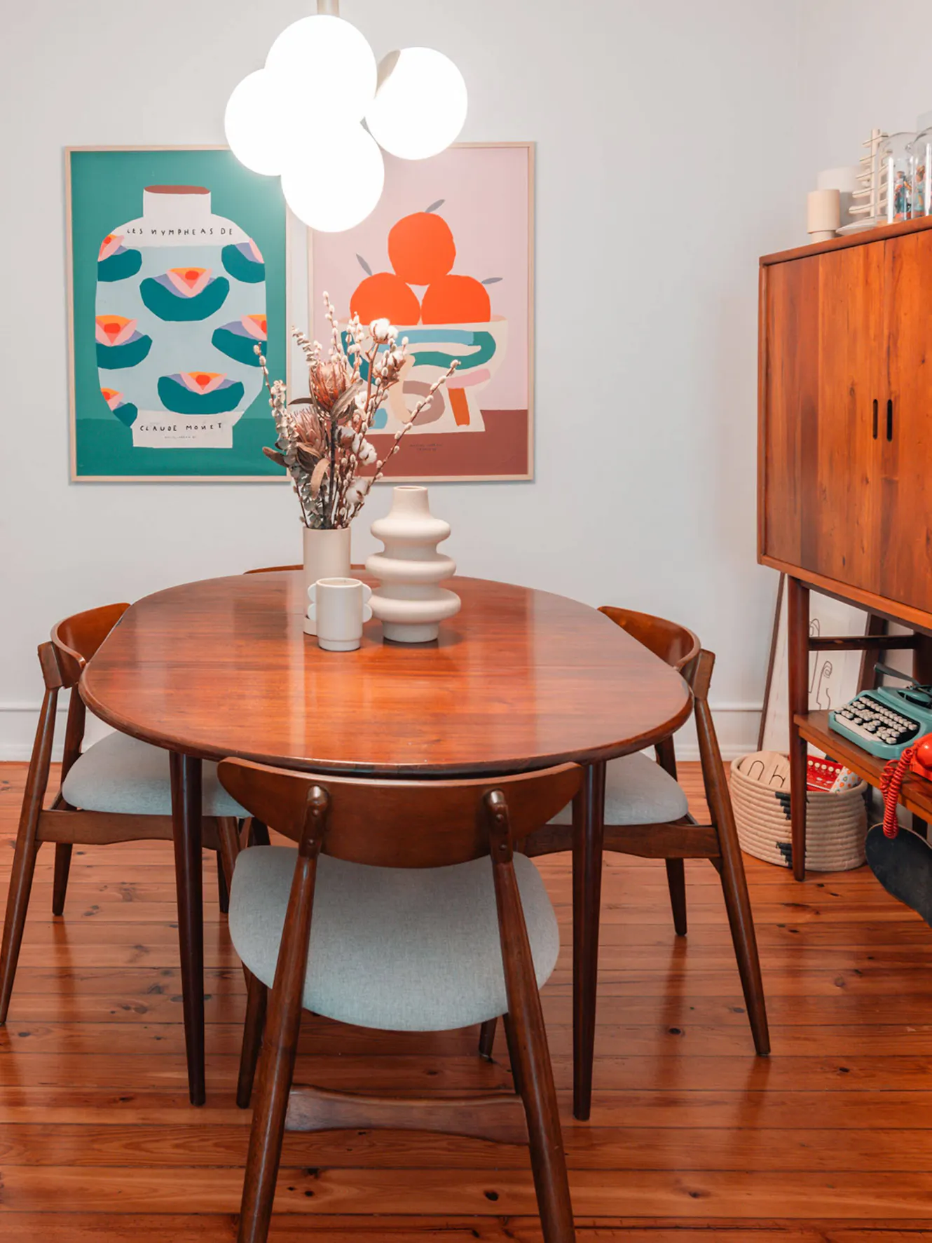 Dining room with round wooden table, four mid-century modern chairs, white cloud pendant light, and colorful abstract artwork on wall