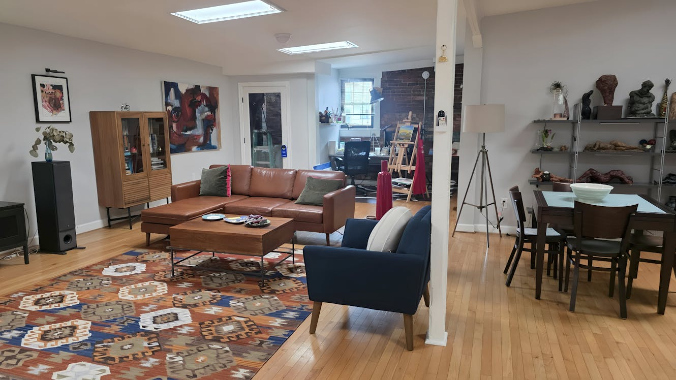 Living room with brown leather sectional sofa, blue armchair, wooden coffee table, skylights, hardwood floors, and colorful patterned area rug
