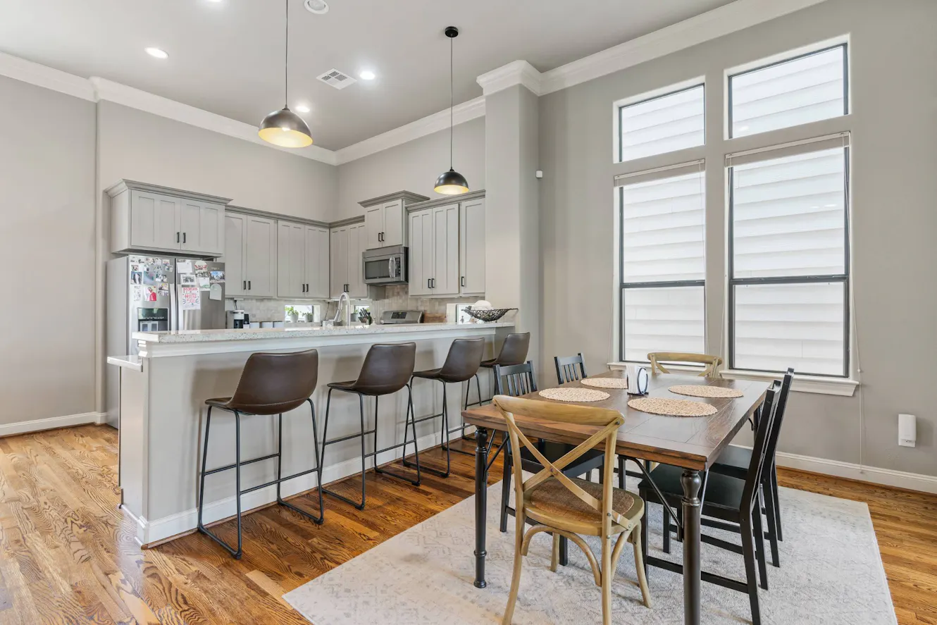 Open concept kitchen and dining area with white cabinets, breakfast bar with four stools, dining table with six chairs, pendant lighting, and large windows
