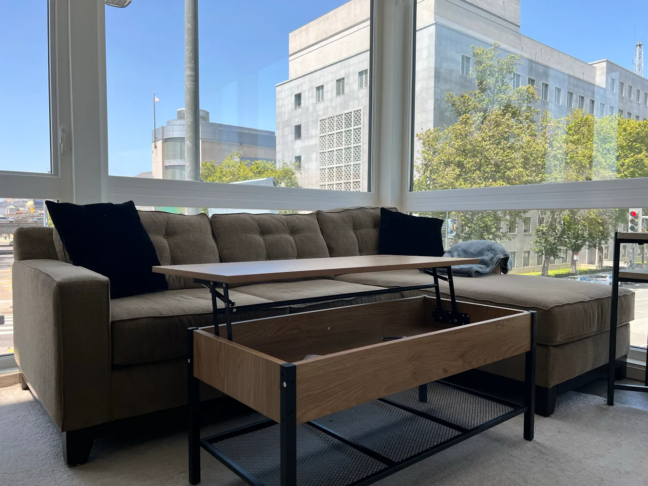 Living room with gray sectional sofa, lift-top coffee table, large windows with city views, and natural light