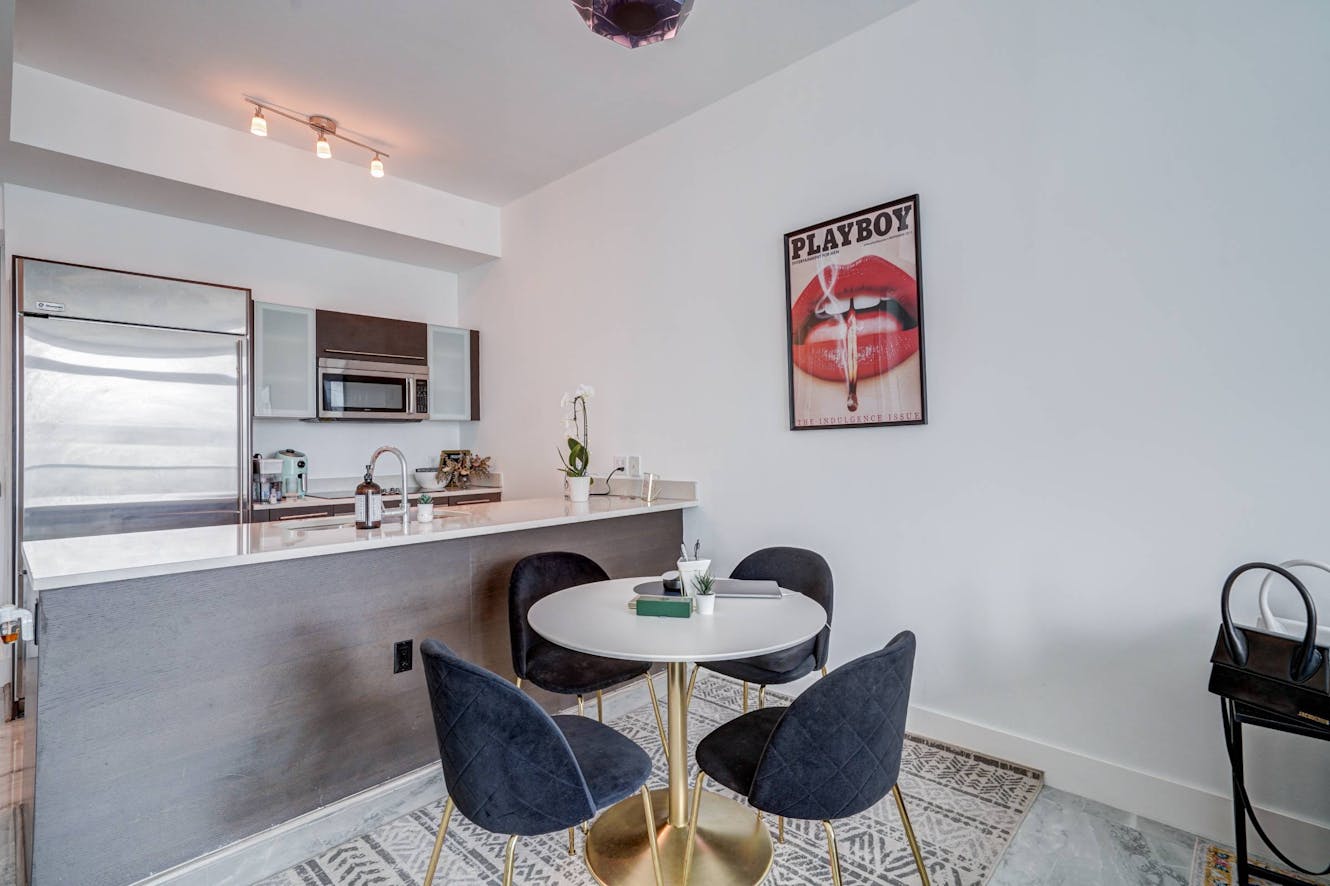 Dining area with white round table, four navy velvet chairs with gold legs, and open kitchen with stainless steel appliances in background