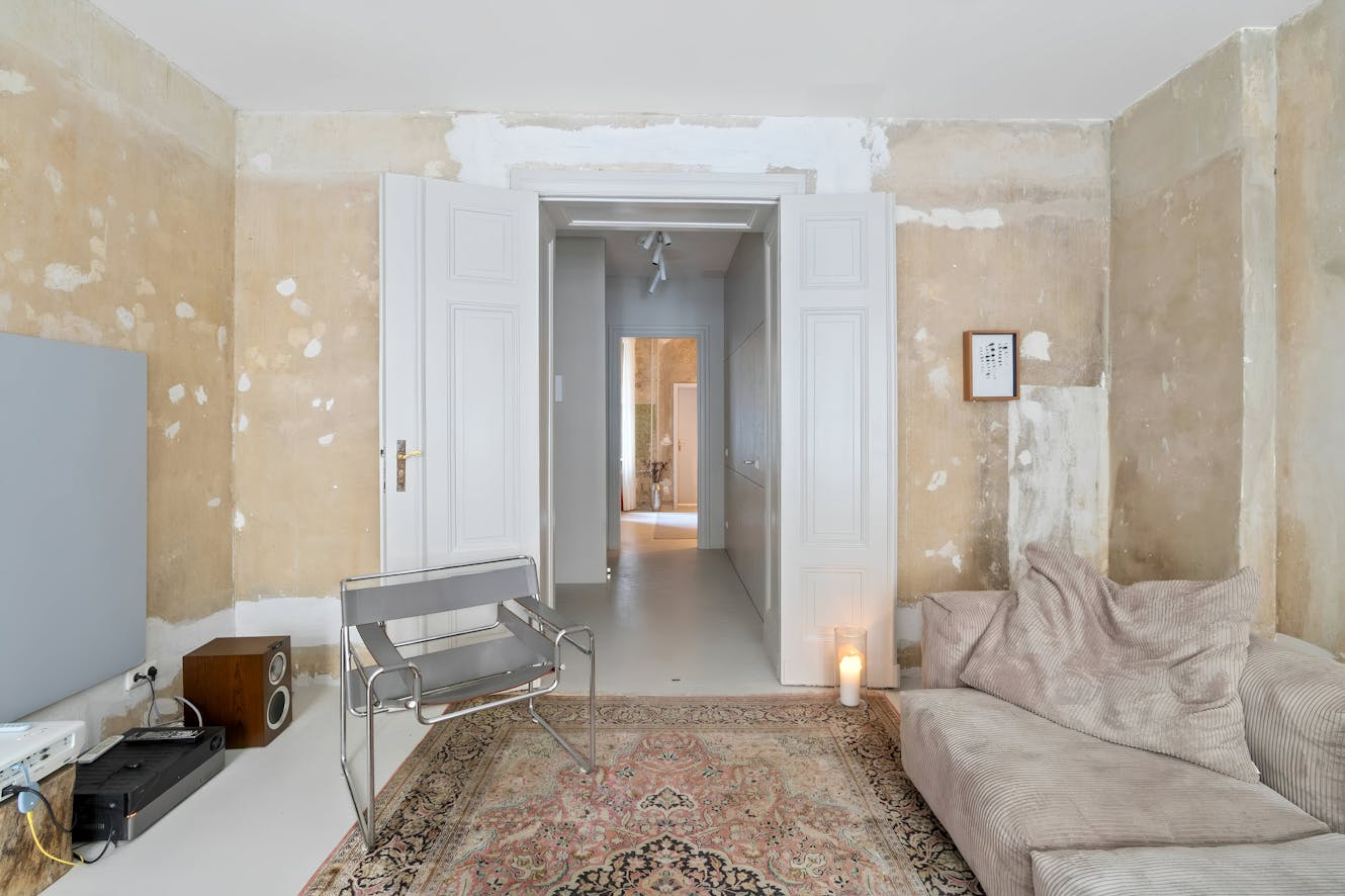Living room with distressed walls, beige corduroy sofa, metal chair, oriental rug, doorway leading to hallway, and vintage stereo equipment