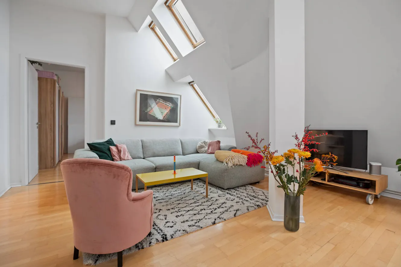 Living room with gray sectional sofa, pink velvet armchair, yellow coffee table, skylight windows, wall-mounted TV, and hardwood flooring