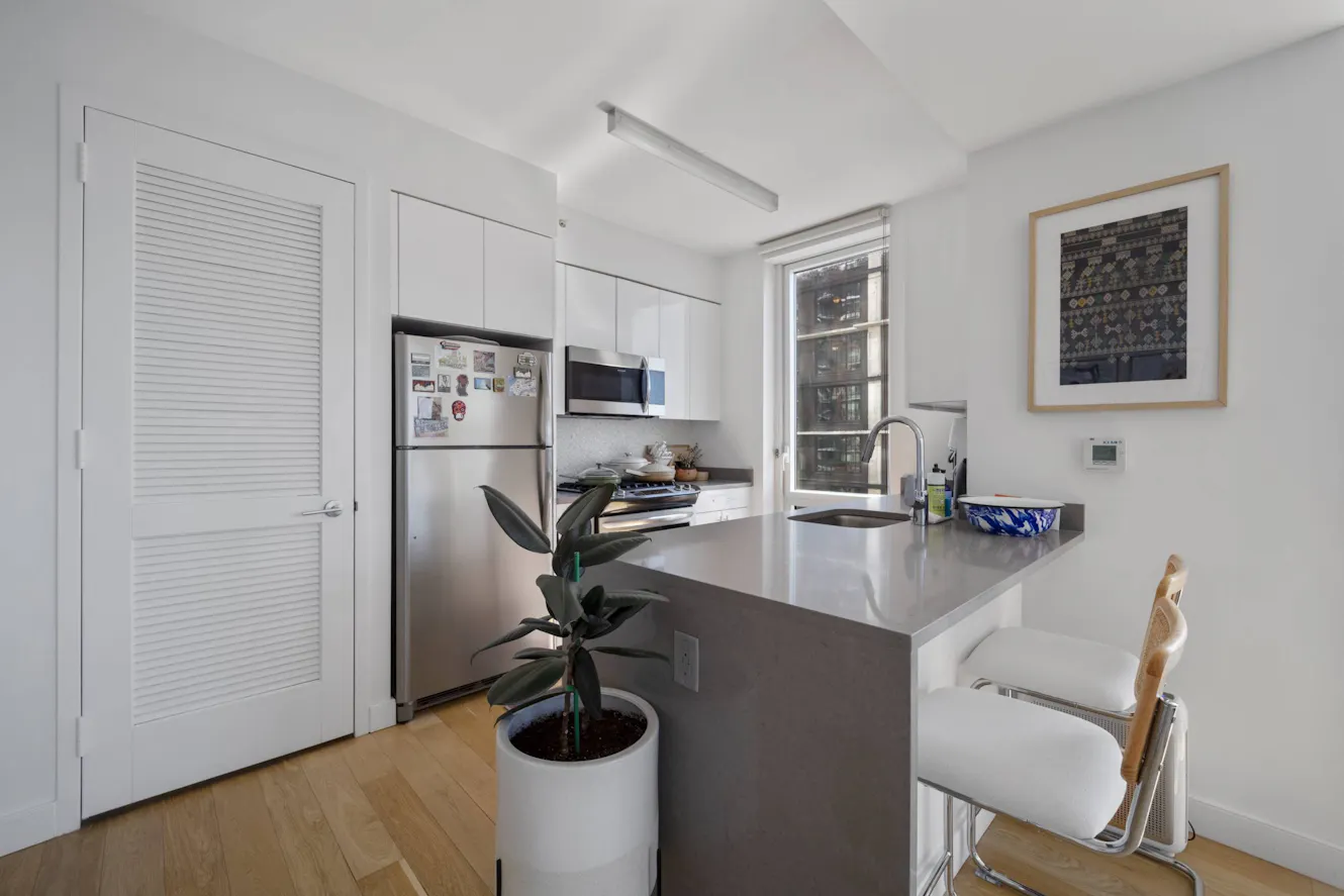 Kitchen with white cabinets, stainless steel appliances, gray countertops, breakfast bar with seating, and window with natural light