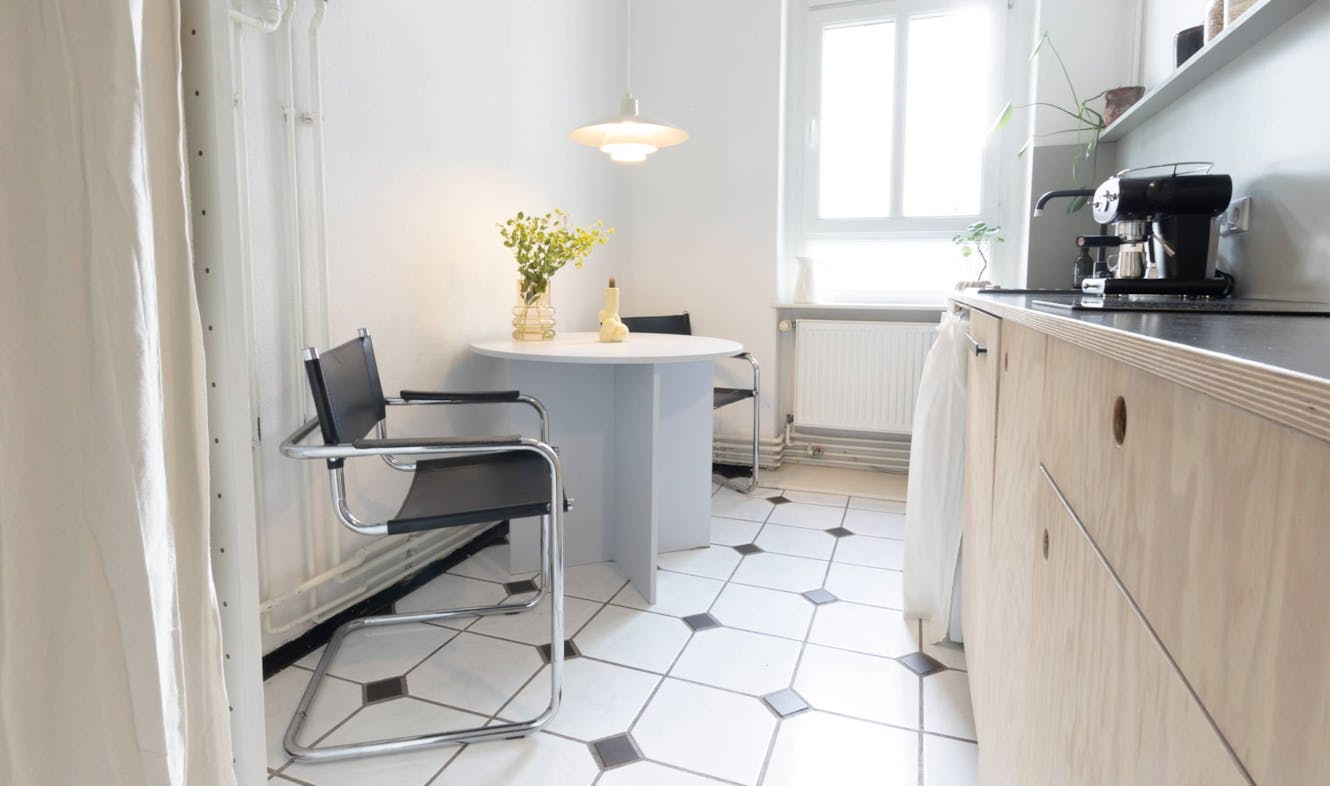 Kitchen with white round dining table, modern black chairs, light wood cabinets, espresso machine, and pendant lighting