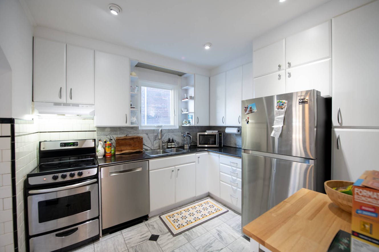 Kitchen with white cabinets, stainless steel appliances including refrigerator and stove, gray countertops, white subway tile backsplash, and window with natural light