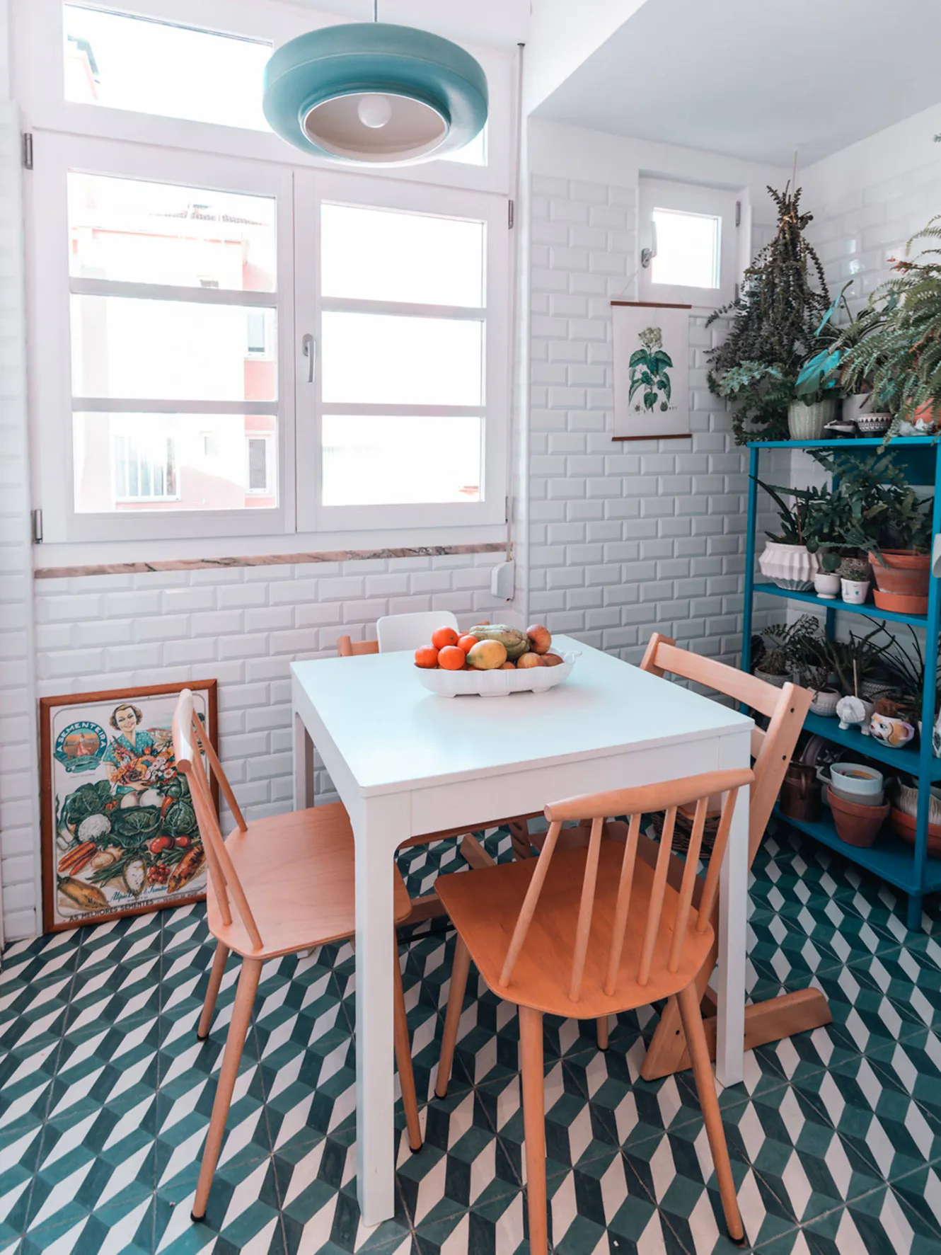 Dining room with white table, wooden chairs, turquoise pendant light, white subway tile walls, large windows, and geometric patterned floor