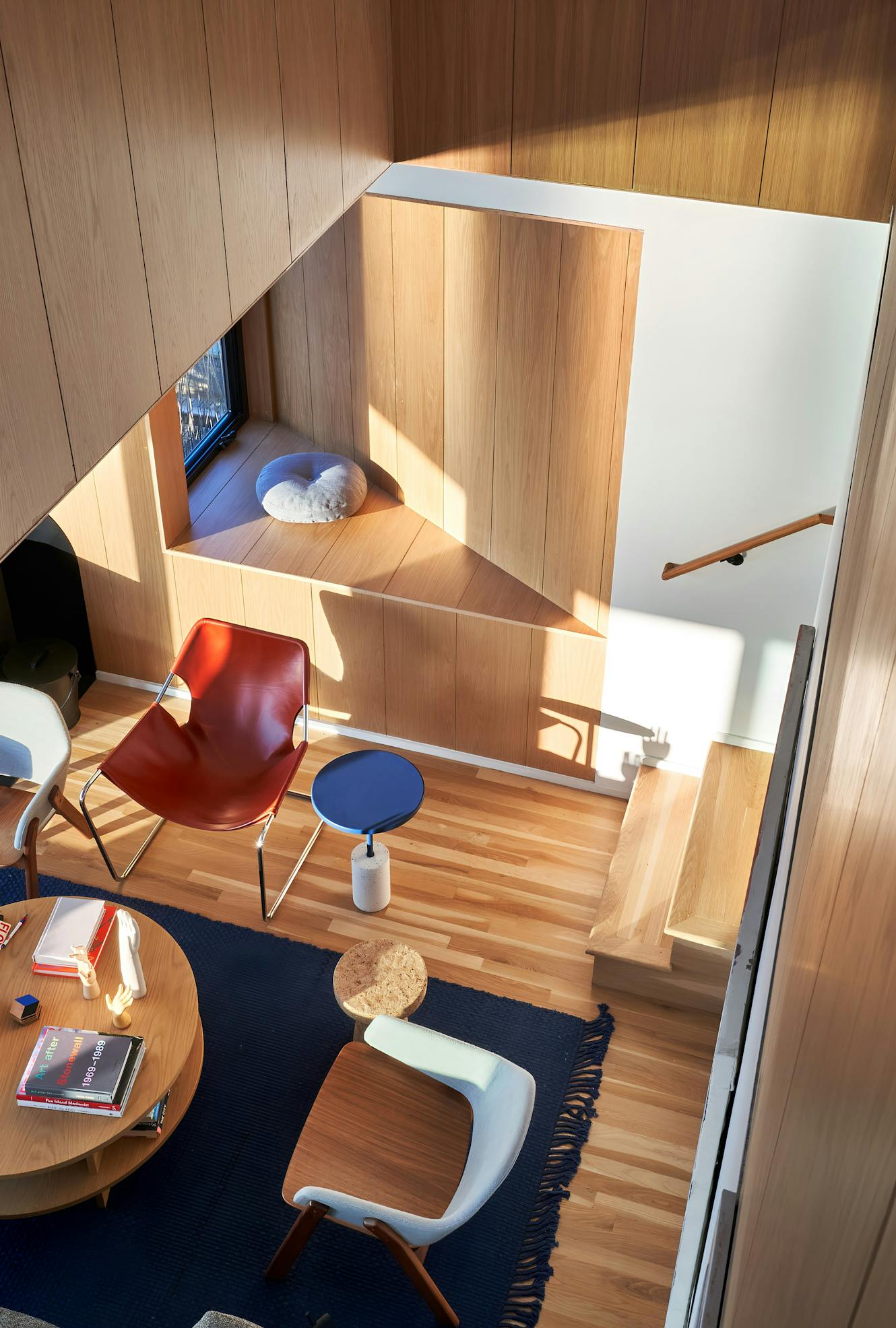 Living room with wood paneled walls, modern chairs, round coffee table, navy area rug, and built-in seating nook with natural light