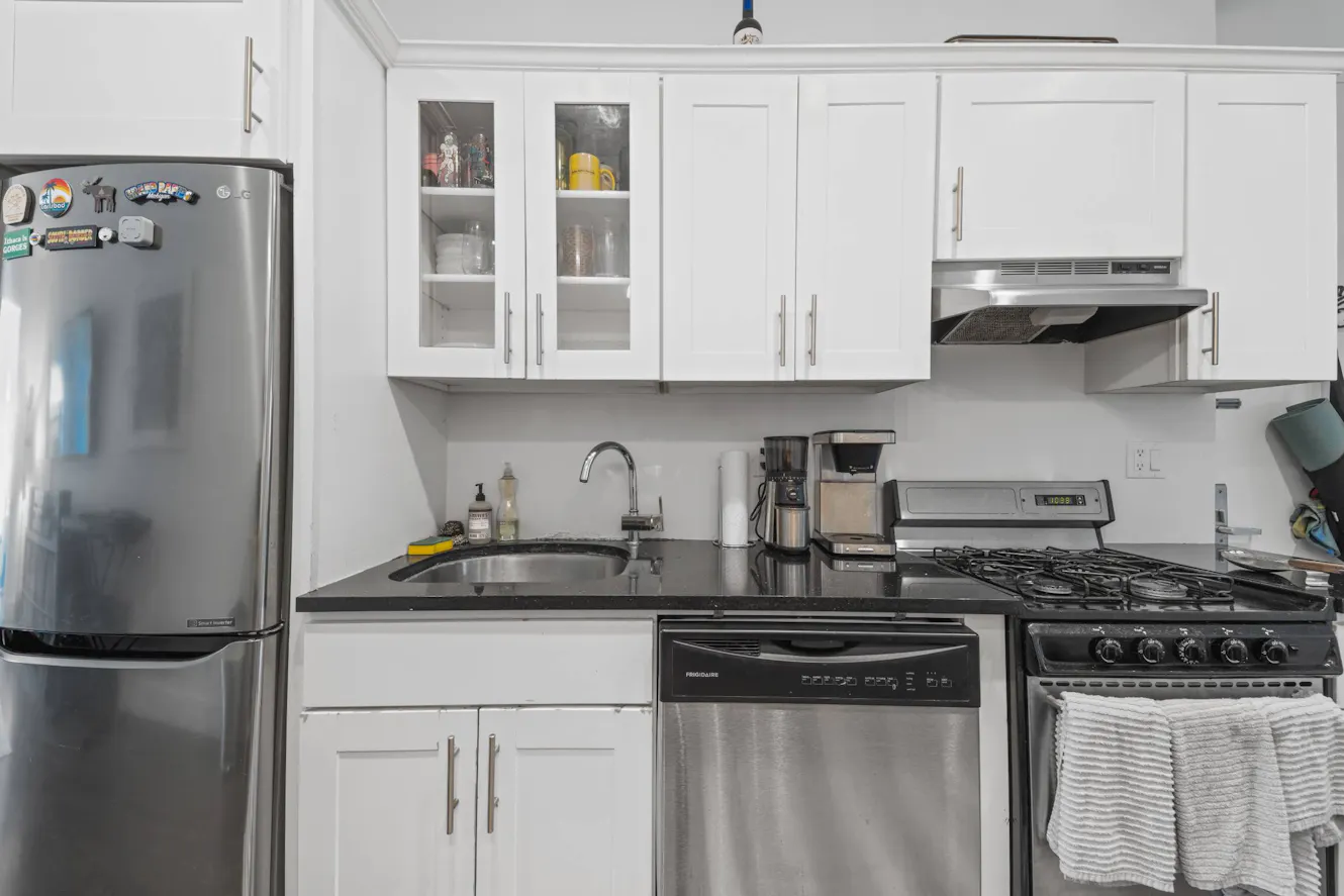 Kitchen with white cabinets, stainless steel appliances including refrigerator, dishwasher, gas range, black granite countertops, and undermount sink