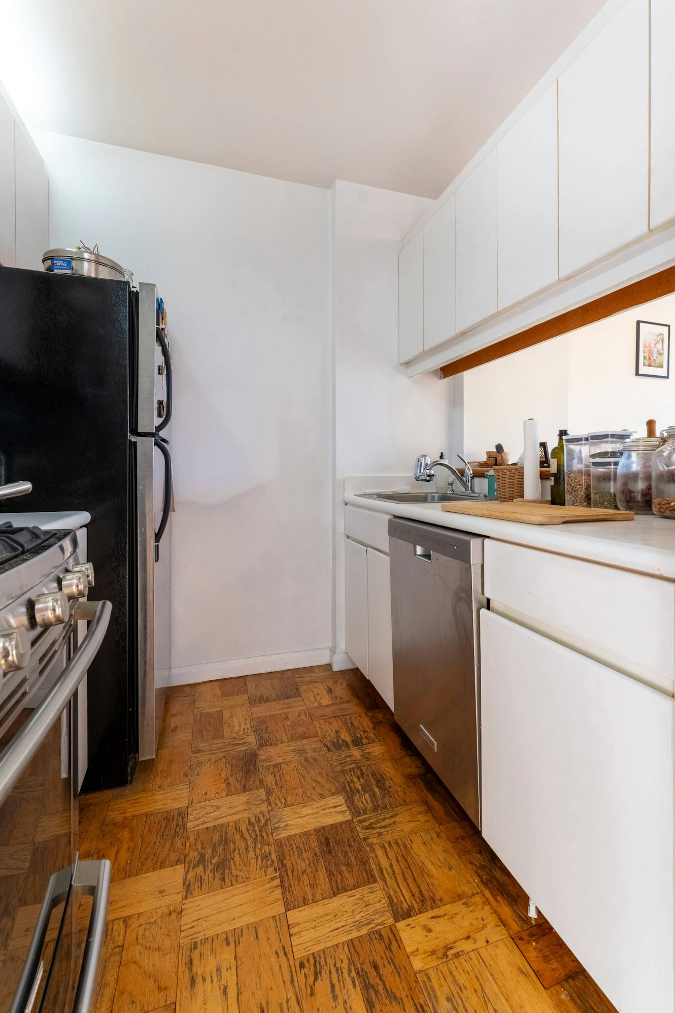 Kitchen with white cabinets, stainless steel appliances including refrigerator and dishwasher, gas stove, sink with countertop, and parquet wood flooring