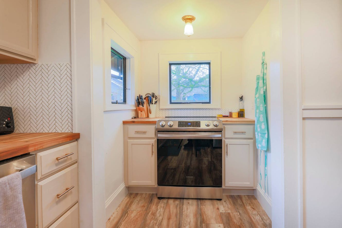 Kitchen with white cabinets, wood countertops, herringbone tile backsplash, stainless steel range, and window with natural light