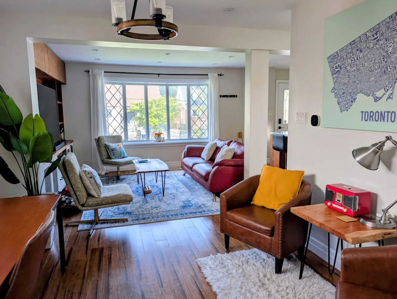 Living room with large window, red leather sofa, brown leather armchair, coffee table, area rug, and Toronto map wall art