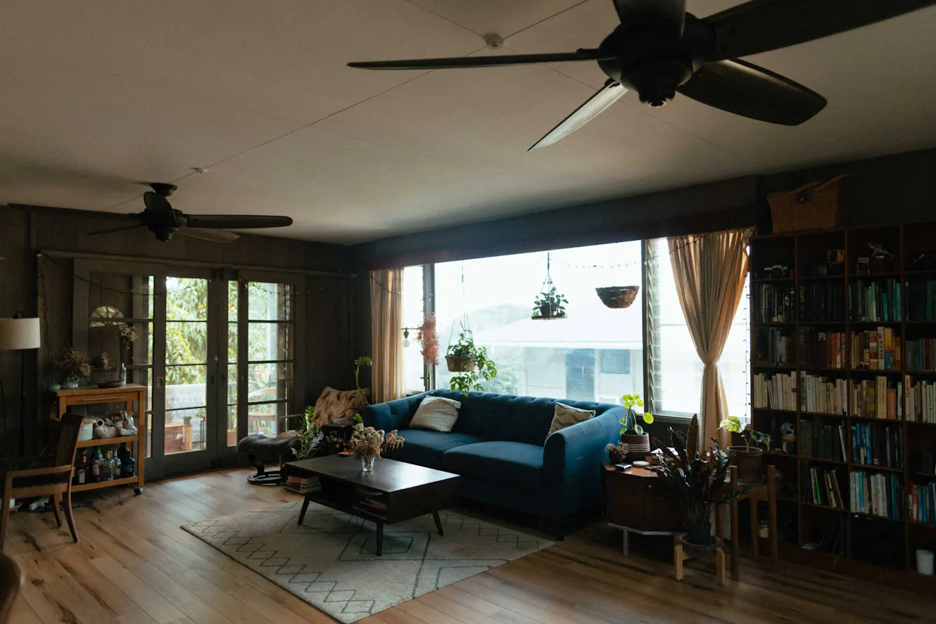 Living room with blue sofa, coffee table, large windows with natural light, French doors, bookshelves, and ceiling fans