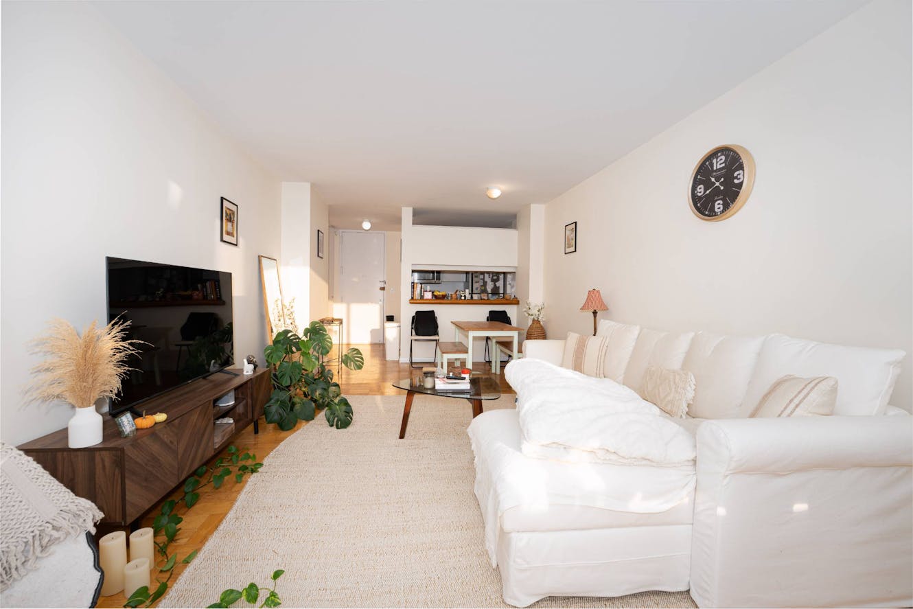 Living room with white sectional sofa, wooden TV console, coffee table, area rug, and open view to dining area and kitchen
