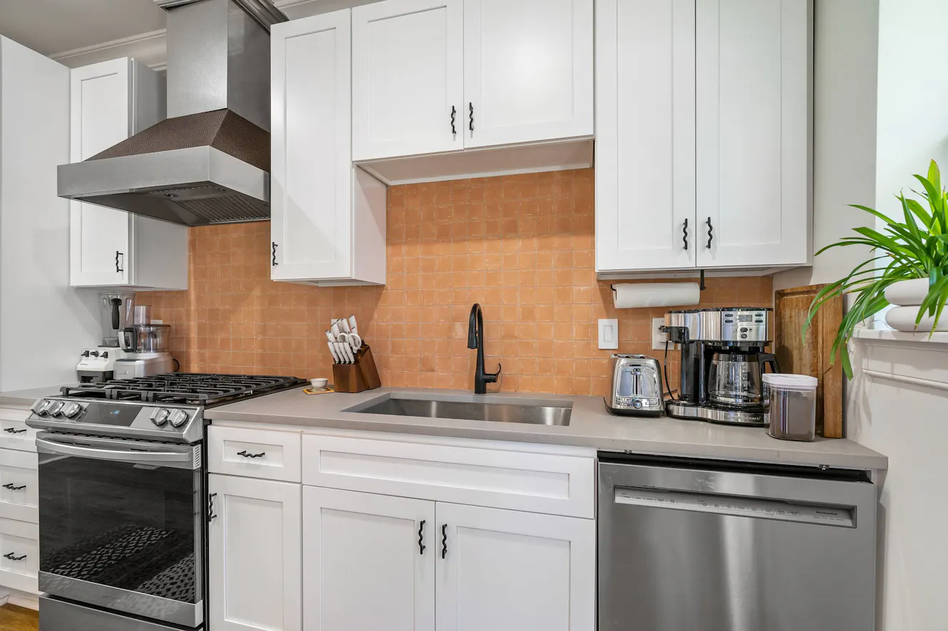 Kitchen with white cabinets, gray countertops, stainless steel appliances, gas range, undermount sink with black faucet, and peach subway tile backsplash