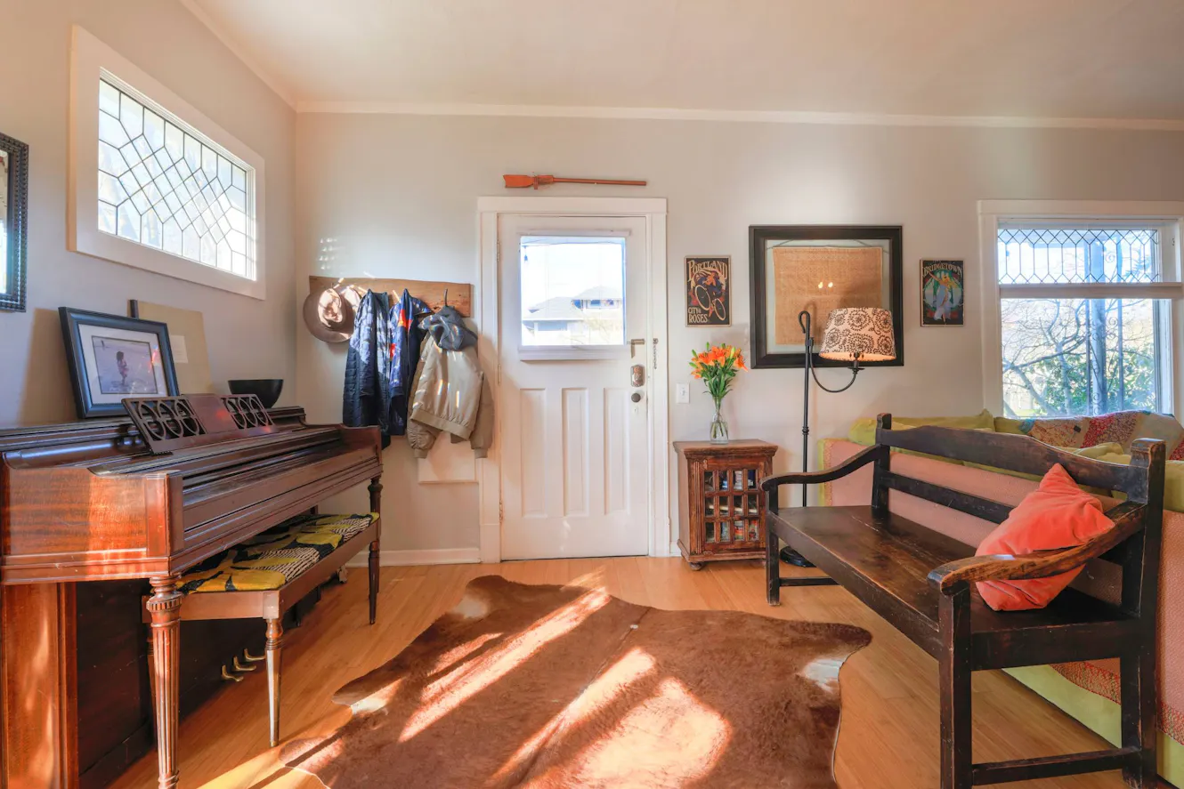 Home entry with white front door, decorative glass windows, hardwood floors, piano, wooden bench with colorful cushions, and wall art