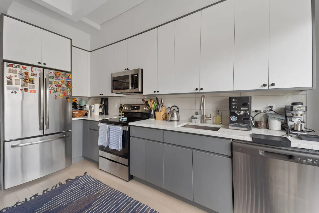 Kitchen with white upper cabinets, gray lower cabinets, stainless steel appliances including refrigerator and dishwasher, undermount sink, and white countertops